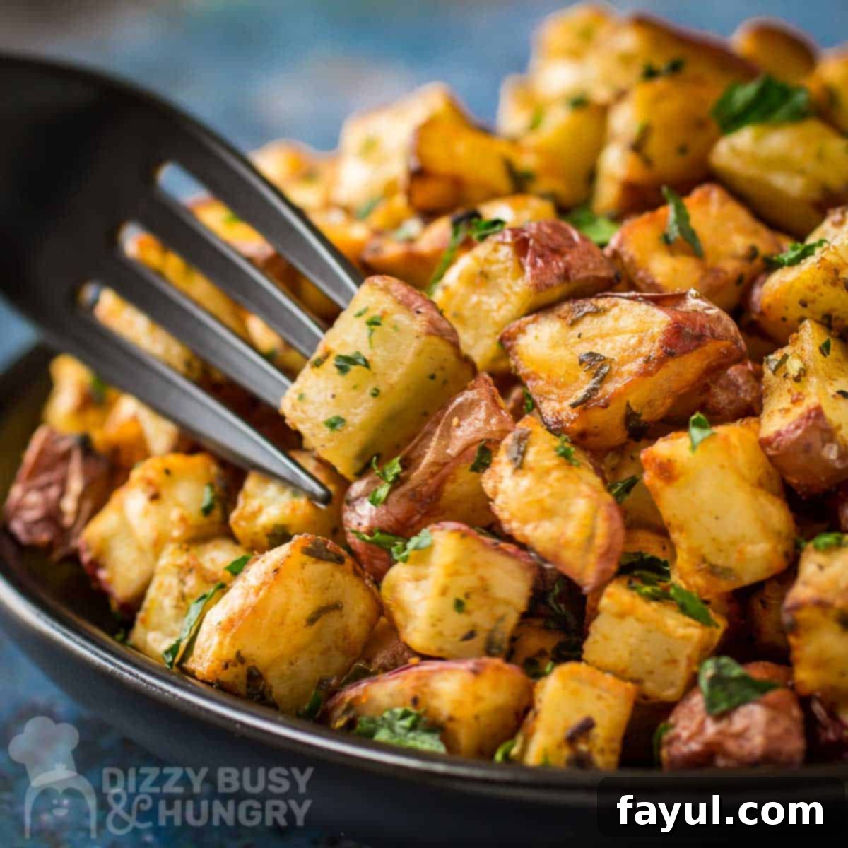 Close up shot of a fork picking up a piece of crispy air fryer breakfast potato from a plate on a blue speckled surface, showing the golden texture.