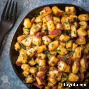Overhead shot of air fryer breakfast potatoes on a black plate on a blue speckled surface with black utensils on the side.