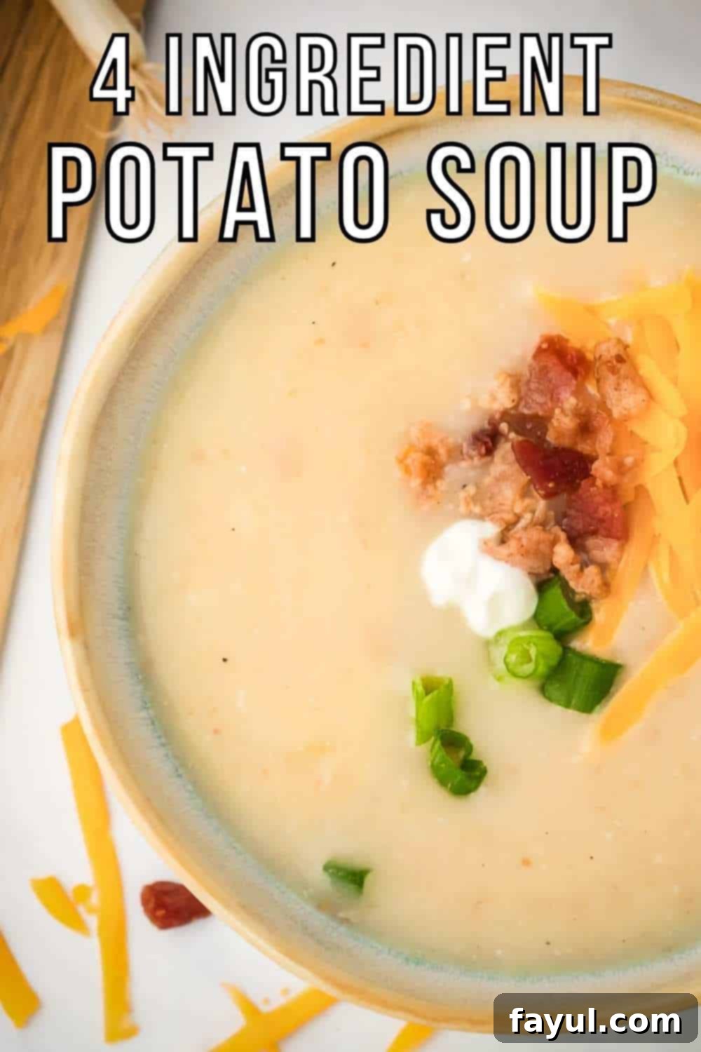 Close up overhead shot of potato soup garnished with shredded cheese, bacon, chives, and sour cream on a white surface.