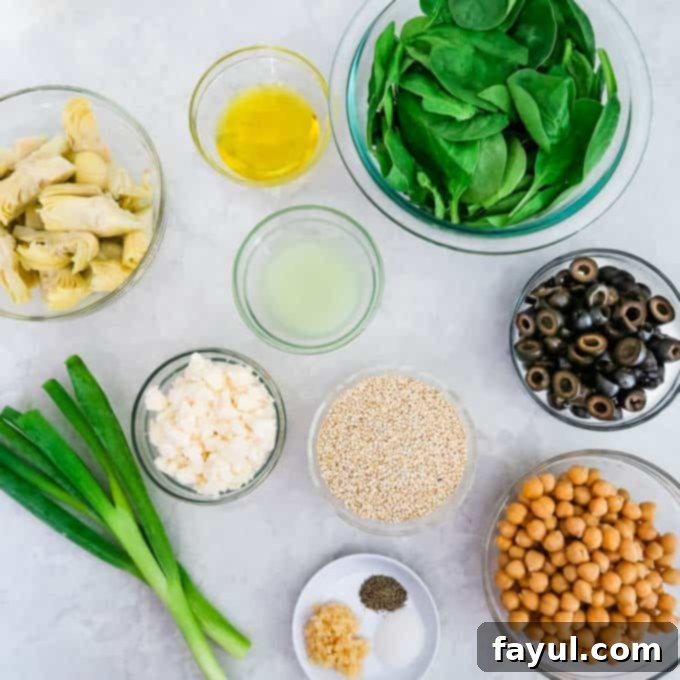 A vibrant flat lay of fresh ingredients for Quinoa Chickpea Salad, including perfectly portioned artichoke hearts, minced garlic, a small bottle of olive oil, lime halves, salt, pepper, canned chickpeas, sliced black olives, a bunch of fresh baby spinach, chopped scallions, and crumbled feta cheese, all artfully arranged and ready for preparation.