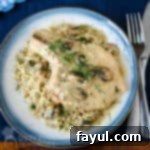 Overhead shot of a tender pork chop, richly covered in a creamy mushroom soup and elegantly garnished with fresh herbs, served on a blue and white patterned plate with silverware neatly arranged on the side, all resting on a dark blue placemat.