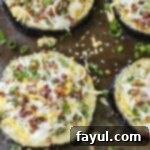 Overhead shot of four loaded eggplant slices, generously topped with cheese and bacon, and garnished with fresh chives, all beautifully arranged on a baking sheet.