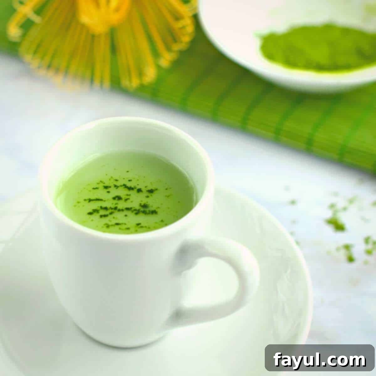 Matcha green tea in a white cup on a white saucer garnished with sprinkled matcha powder on the surface of the tea.