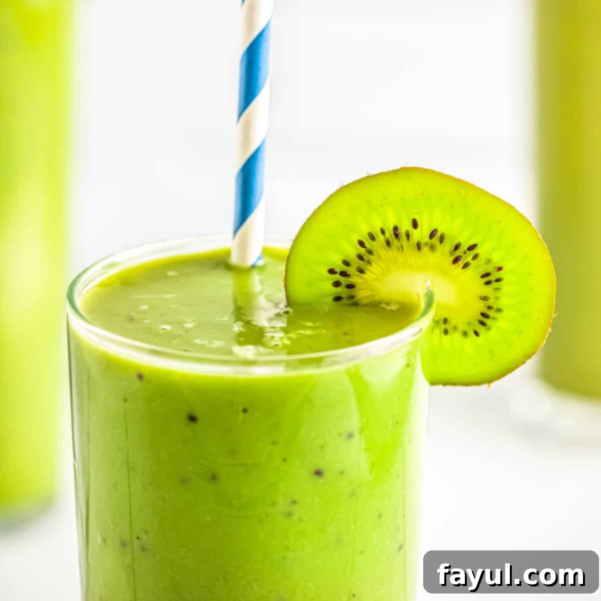 Close up photo of a glass with matcha kiwi smoothie, garnished with a slice of kiwi and a blue and white straw.