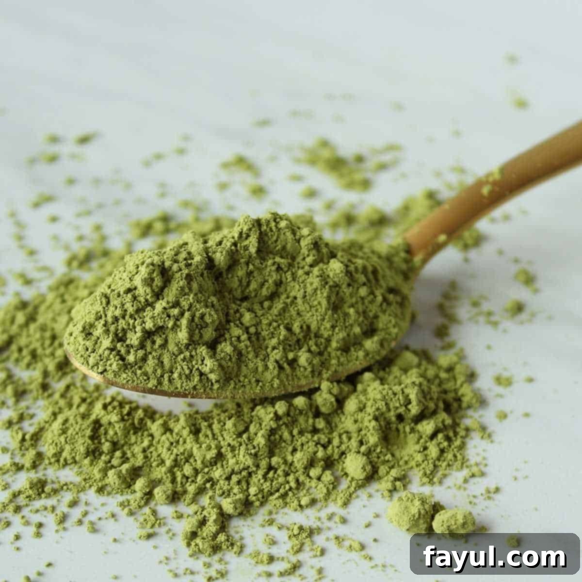 Green tea powder on a wooden spoon spilling over onto a white surface.
