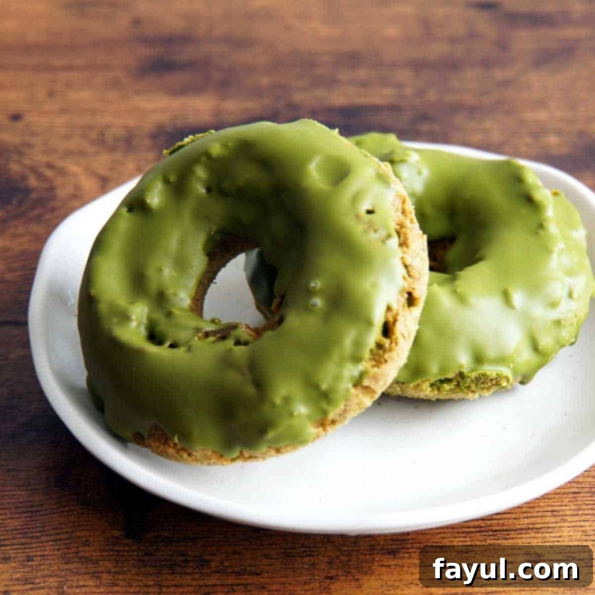 Two matcha baked doughnuts with matcha glaze on a white plate.