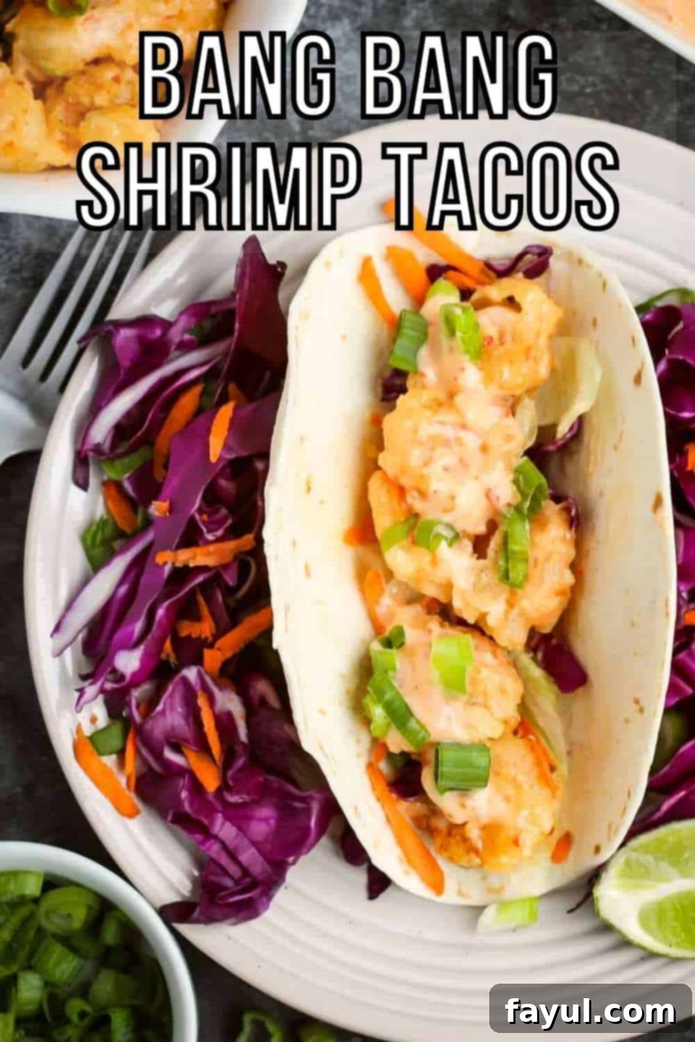 Overhead shot of one shrimp taco with shredded carrots and purple cabbage surrounding it and a lime wedge on the side of the white plate. On the black surface surrounding, there is more shrimp, sauce, and chopped green onions in white bowls as well as a fork and grey cloth.