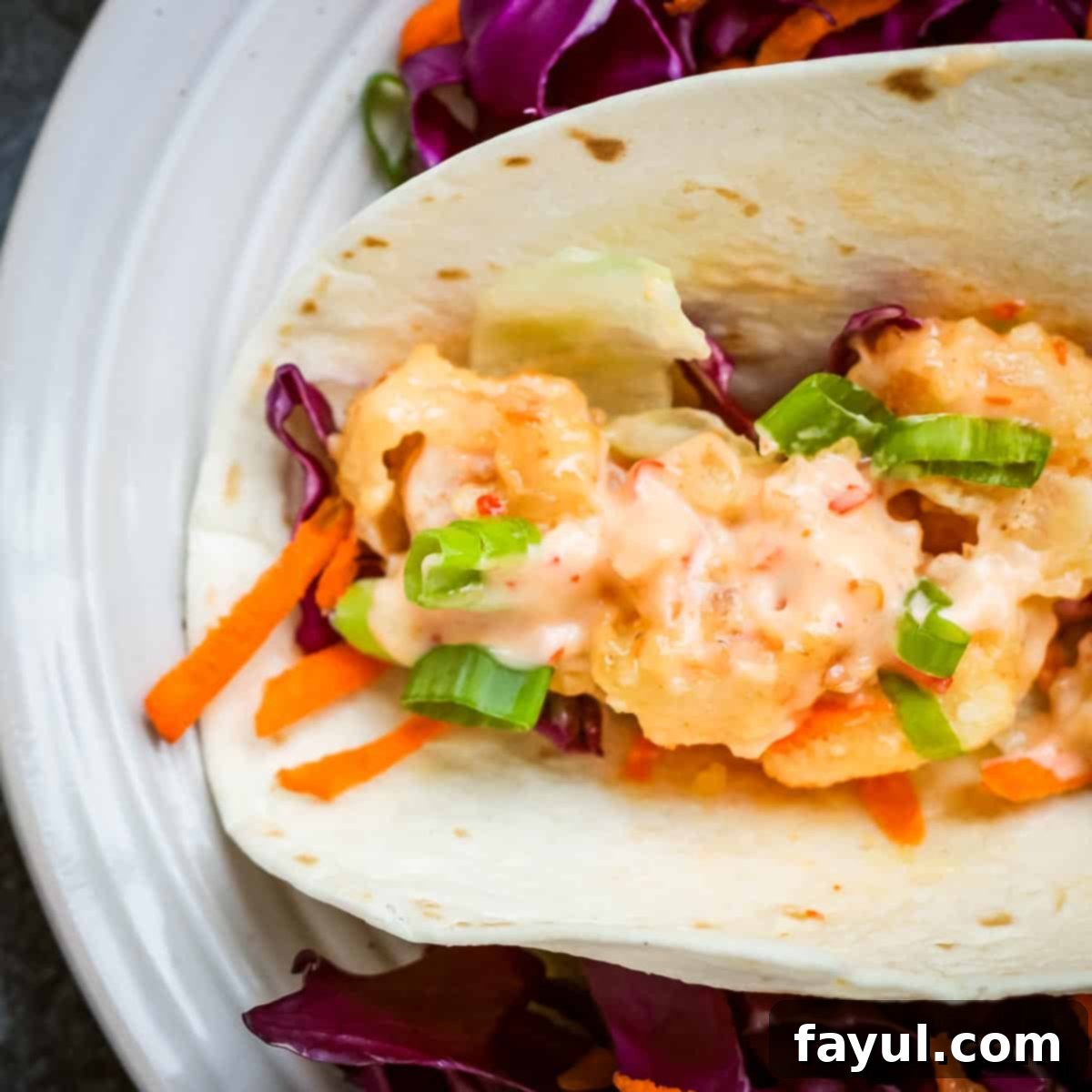 Overhead close up shot of a shrimp taco with shredded carrots and cabbage on a white plate.