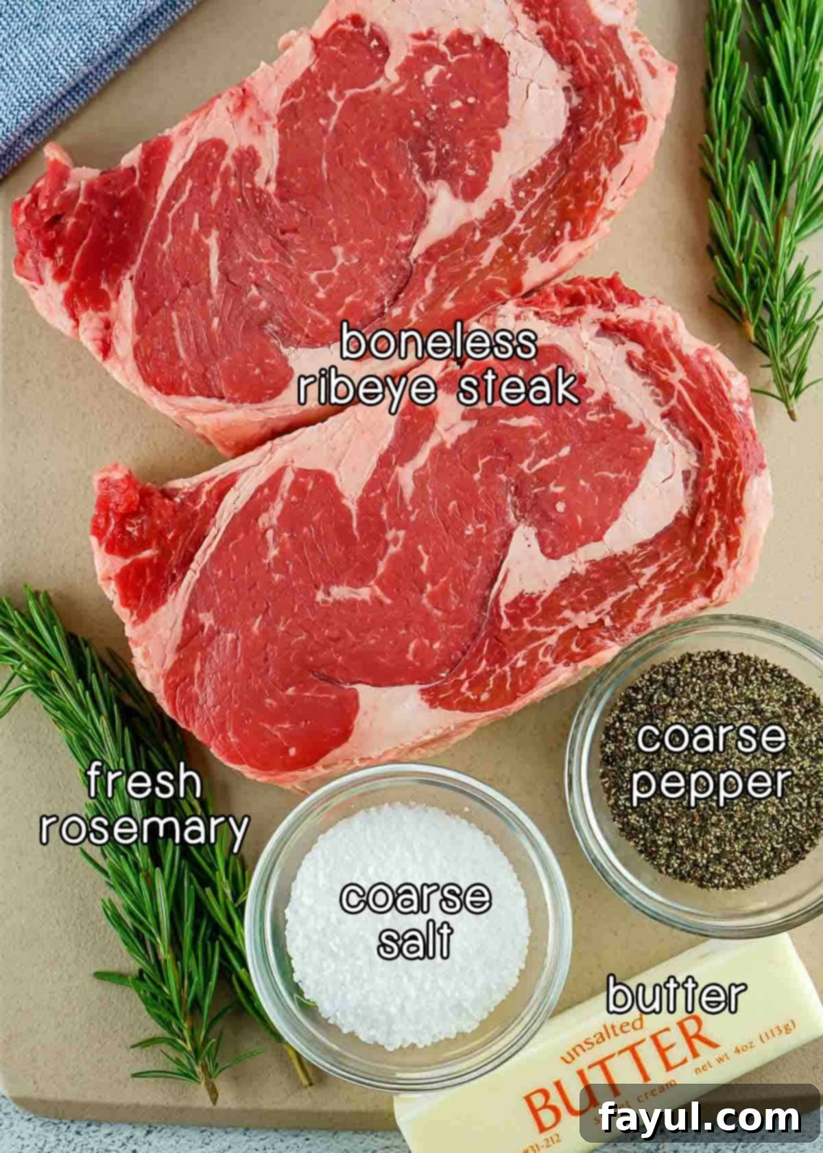 Overhead shot of ingredients - boneless ribeye steak, fresh rosemary, coarse salt, coarse pepper, and butter.