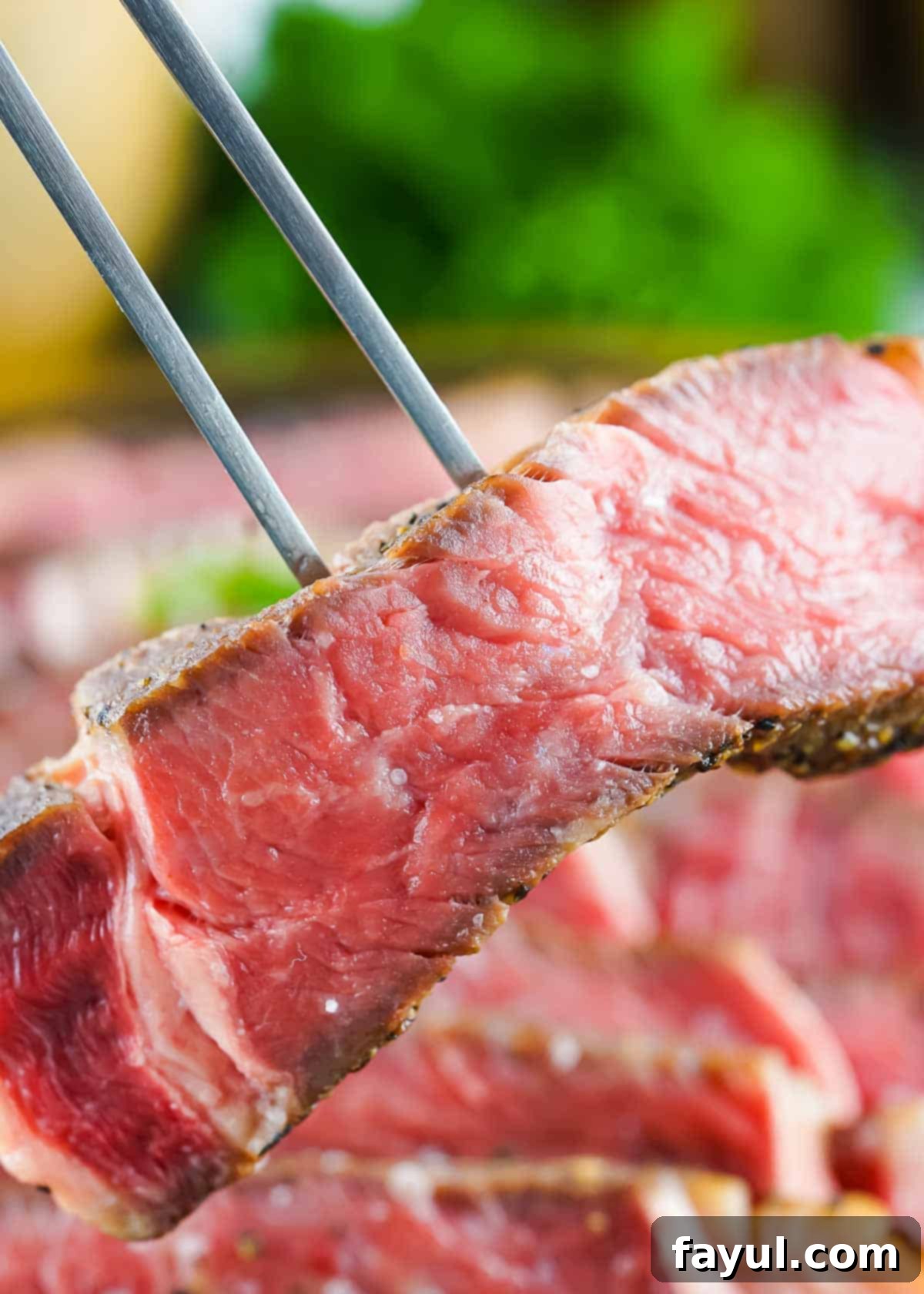 Close up shot of a two pronged fork holding up a slice of rare ribeye with more slices blurry in the background.