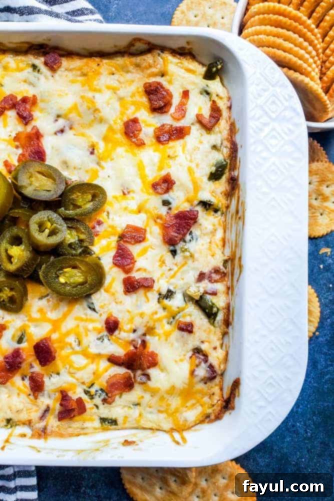 This Baked Bacon Jalapeno Popper Dip with Bacon is the best, easy appetizer recipe! Perfect for game days, parties, holidays or just for the family and ready in only 30 minutes. Pair with tortilla chips, Ritz Crackers or Veggie Sticks for the perfect finish. Simple step by step instructions for crockpot and oven, recipe alterations, and video included! #dip #cheese #JalapenoDip #Spicy #bacon #appetizer #recipe #gamedays #Thanksgiving #Christmas Overhead shot of jalapeno dip in white baking dish.