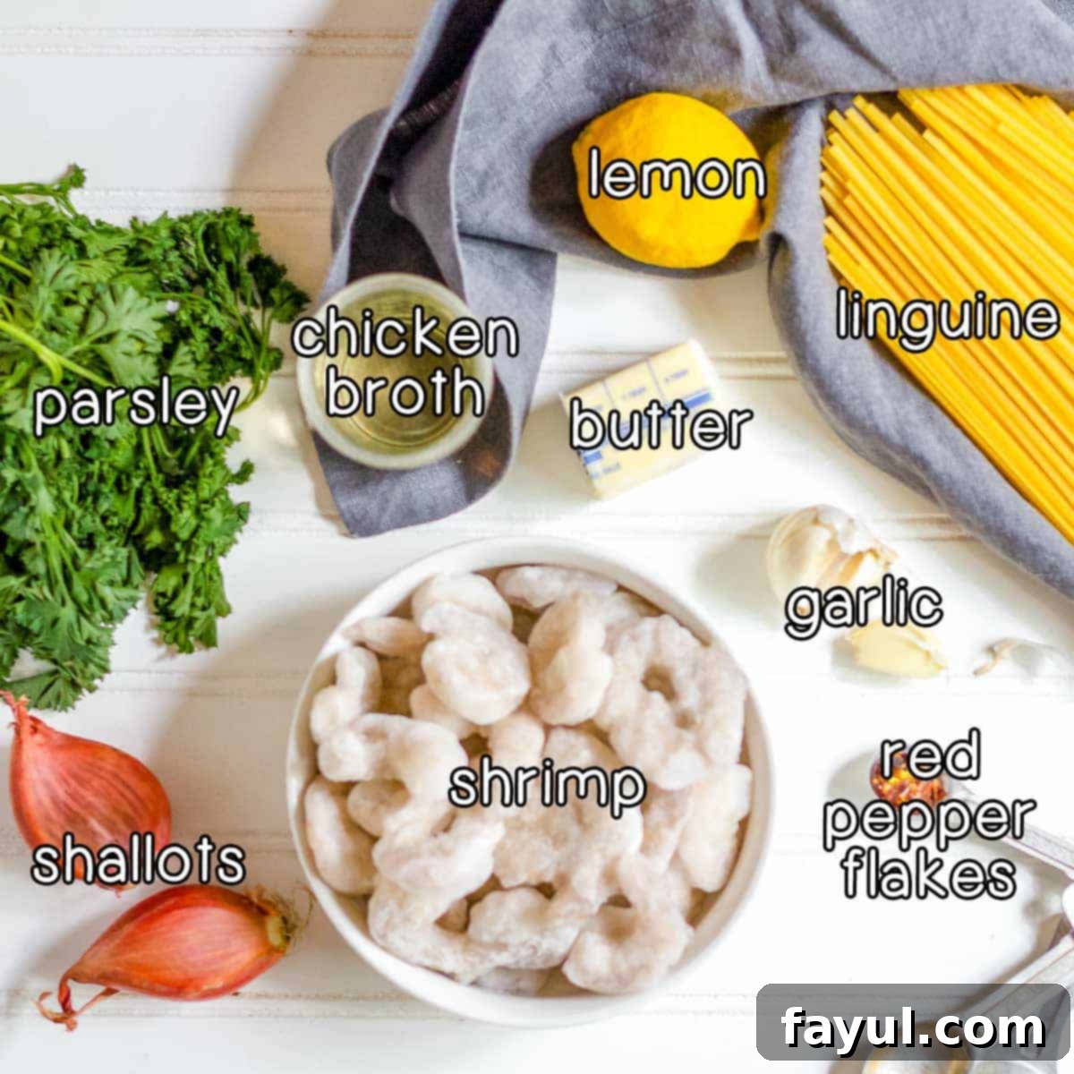 Overhead shot of all the key ingredients needed for shrimp scampi without wine: fresh parsley, finely chopped shallots, chicken broth, a bright yellow lemon, creamy butter, linguine pasta, minced garlic, a sprinkle of red pepper flakes, and raw shrimp.