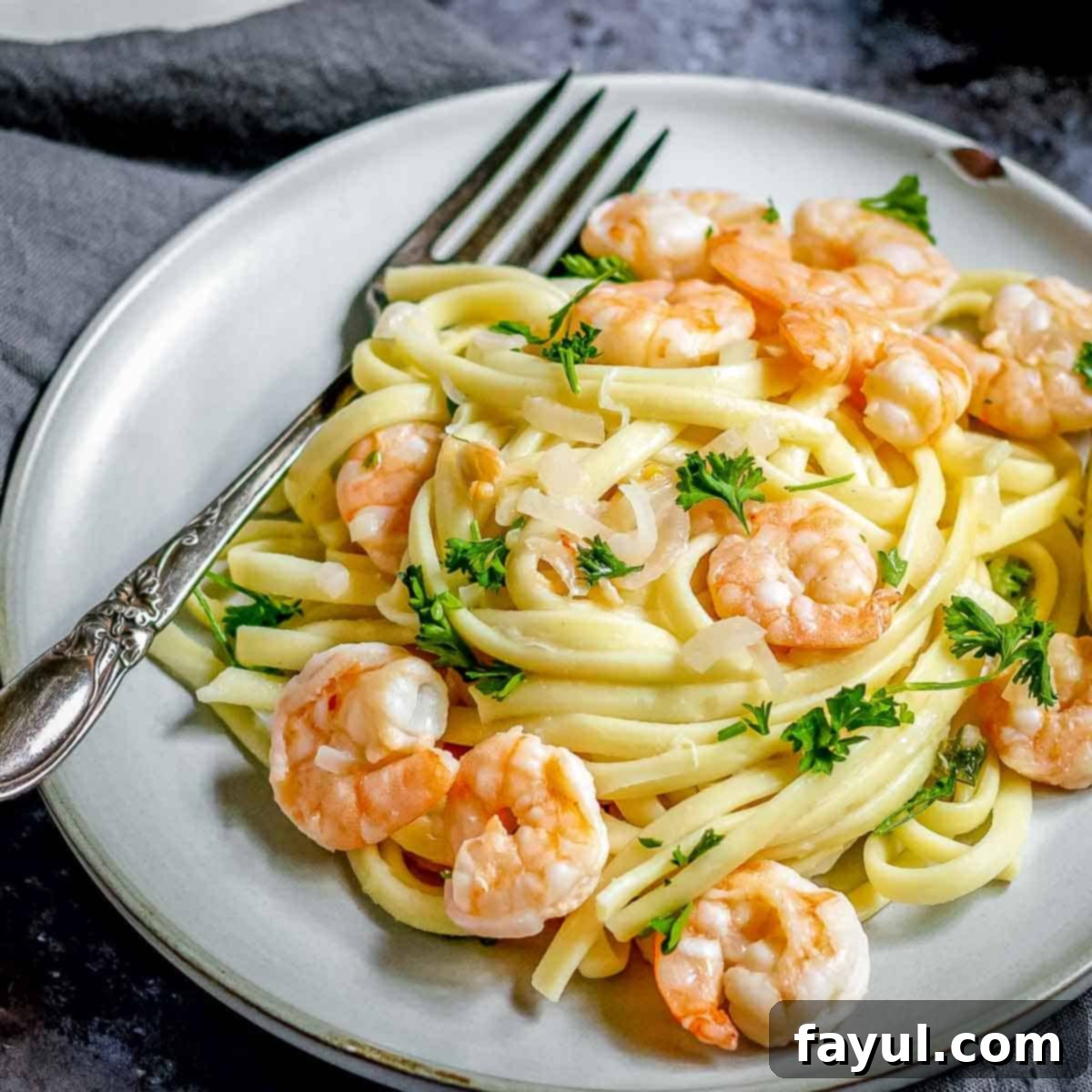 Side close-up shot of the finished shrimp scampi, beautifully garnished with fresh parsley on a grey plate, with a fork resting beside it on a black and grey surface. The dish highlights the tender shrimp and rich sauce.