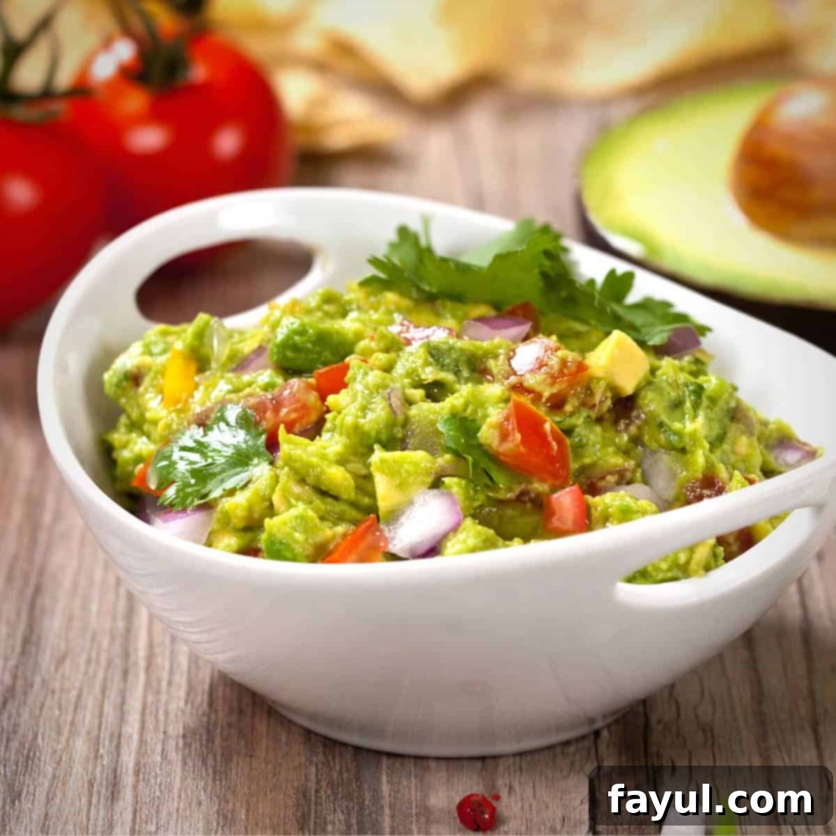 Avocado Flavor Demystified 7 Guacamole in a white bowl on a wooden surface with red tomatoes and an avocado half visible in the background.