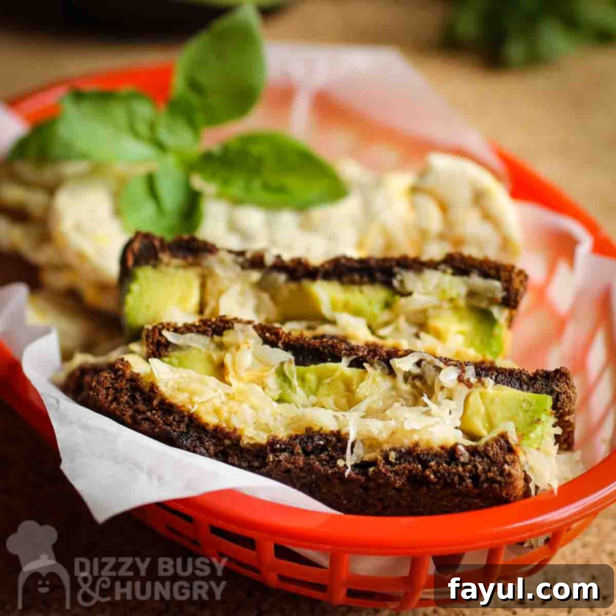 Avocado Flavor Demystified 8 Side angled shot of one sandwich split in half in a red basket lined with parchment paper with herbs on the side.