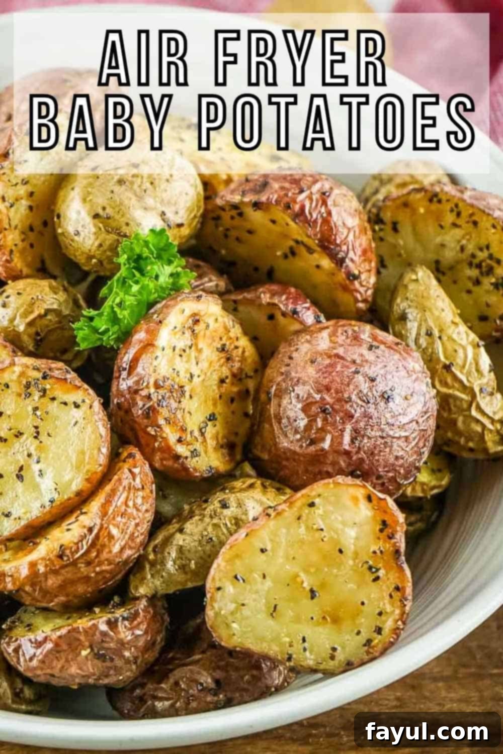 Crispy Air Fryer Baby Potatoes 2 Side angled shot of halved baby potatoes garnished with fresh herbs in a white bowl on a wooden surface.