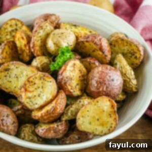 Crispy Air Fryer Baby Potatoes 7 Side angled shot of halved baby potatoes garnished with fresh herbs in a white bowl on a wooden surface.