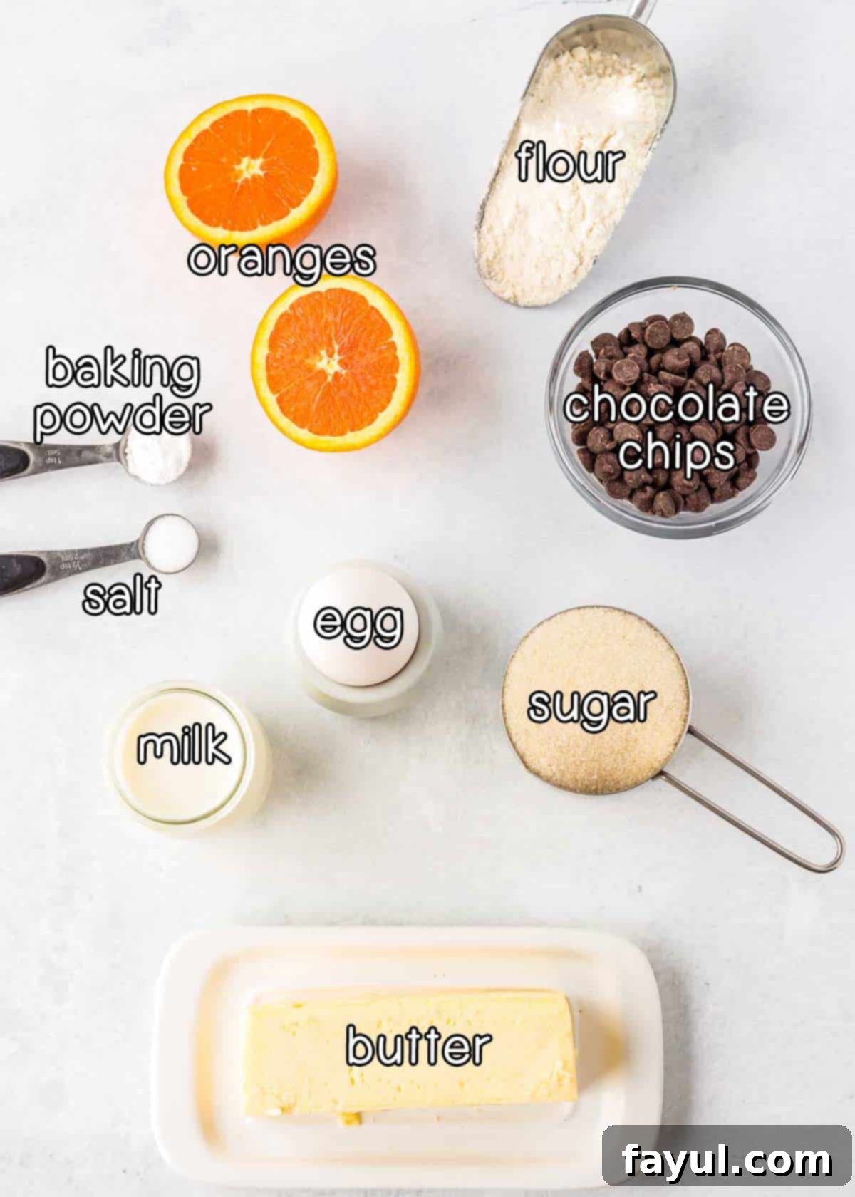 Overhead shot of all ingredients laid out neatly: flour, fresh oranges, baking powder, salt, milk, egg, sugar, semi-sweet chocolate chips, and melted butter.