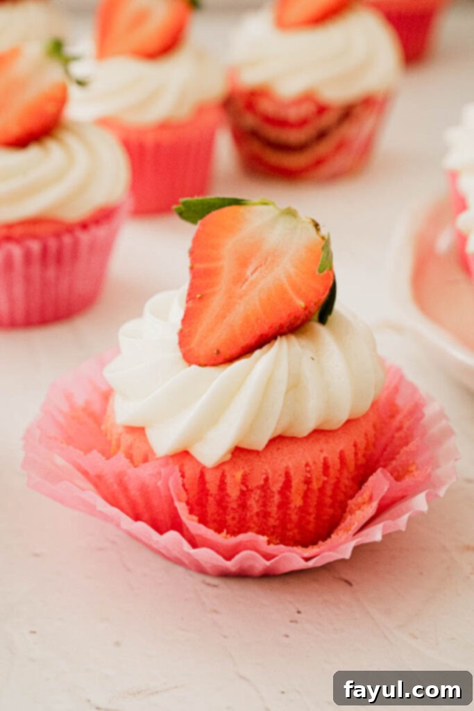 A close-up of a strawberry marshmallow cupcake with a perfect swirl of frosting and a fresh berry.