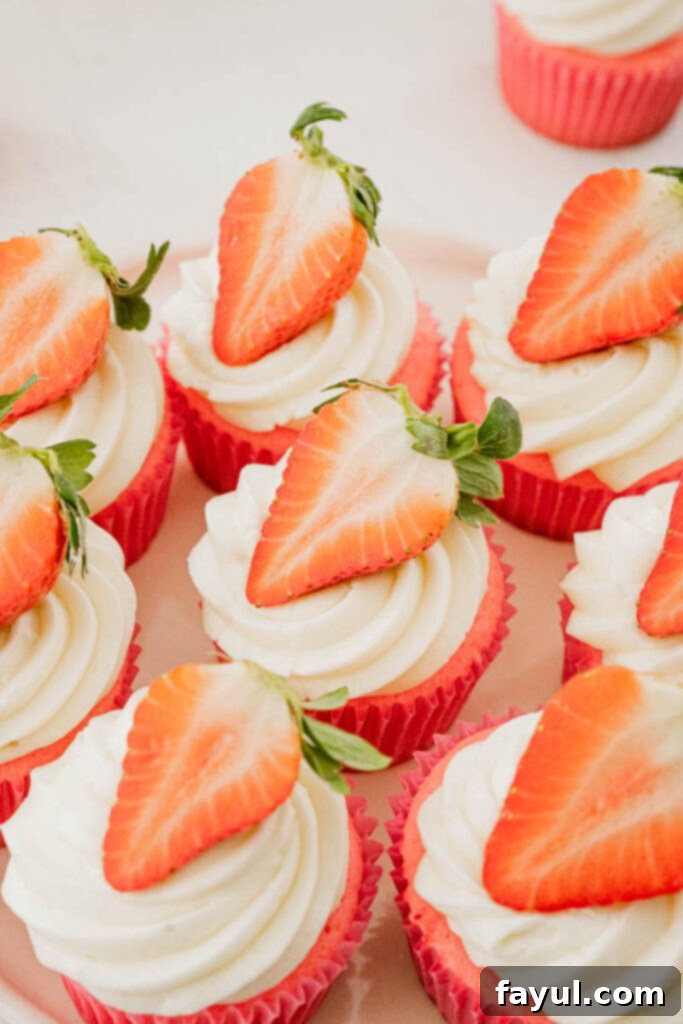 Close-up of a perfectly baked strawberry cupcake with marshmallow buttercream and a fresh strawberry garnish.