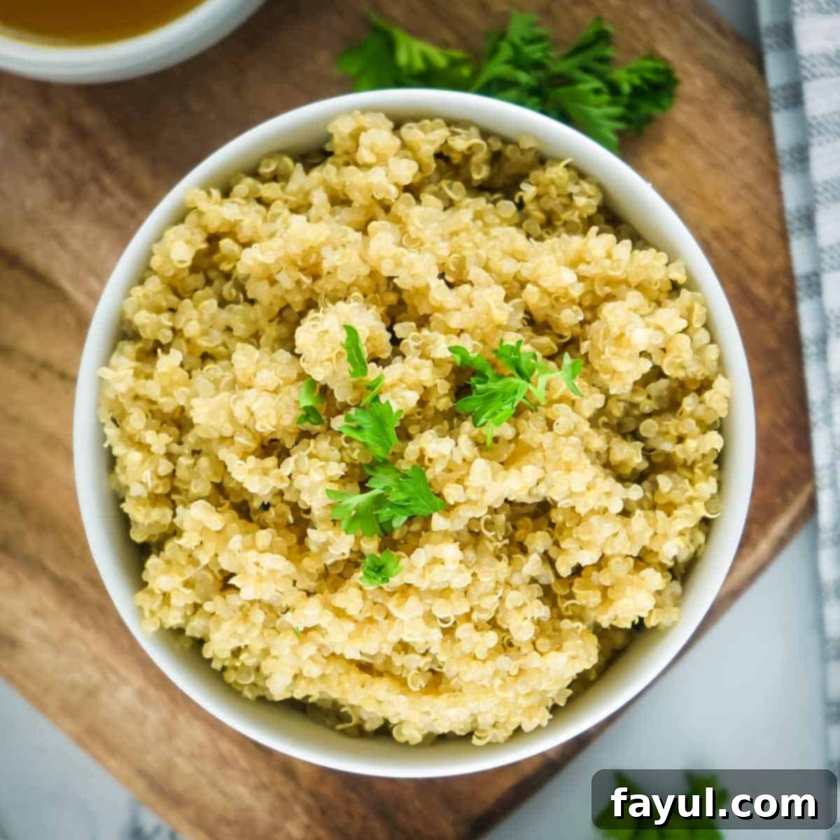 Fluffy Instant Pot Quinoa 5 Overhead shot of a white bowl of fluffy quinoa garnished with fresh herbs on a wooden cutting board.