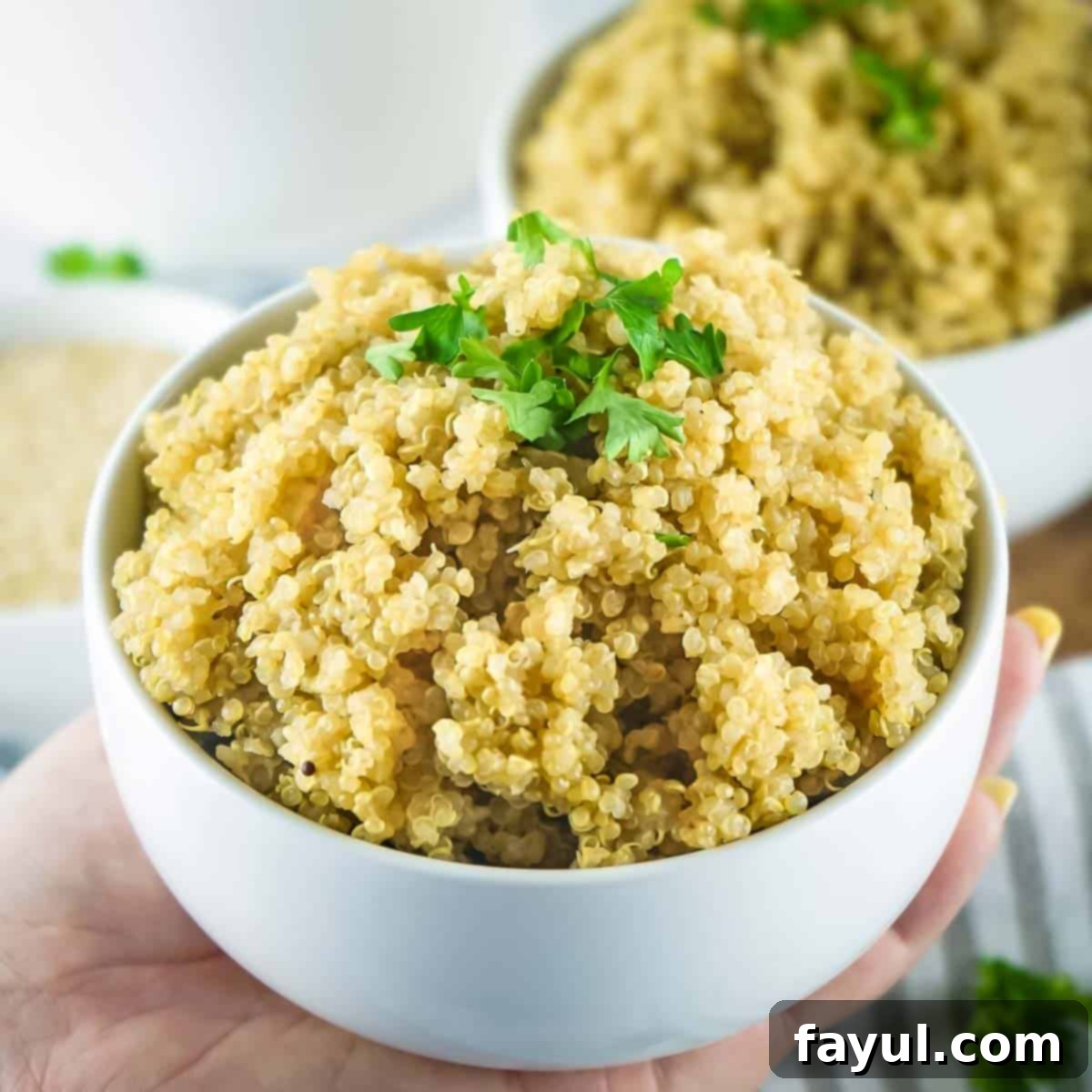Fluffy Instant Pot Quinoa 6 Side shot of a hand holding a small white bowl of quinoa garnished with fresh herbs with more bowls in the background.