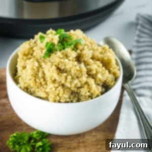 Fluffy Instant Pot Quinoa 7 Side shot of a white bowl of fluffy quinoa garnished with fresh herbs on a wooden surface with a spoon and cloth napkin on the side.