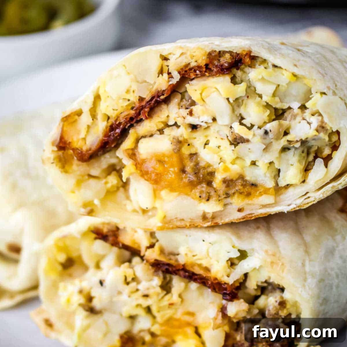 Side close up shot of a cross section of a breakfast burrito on a white plate with more in the background.
