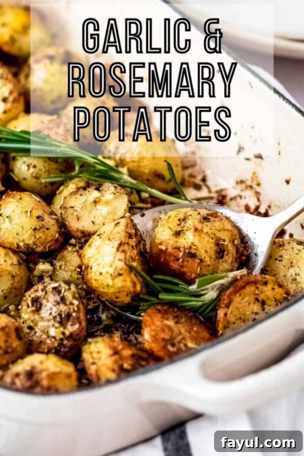Side shot of a spoon picking up a few potatoes from a white pan garnished with fresh rosemary.