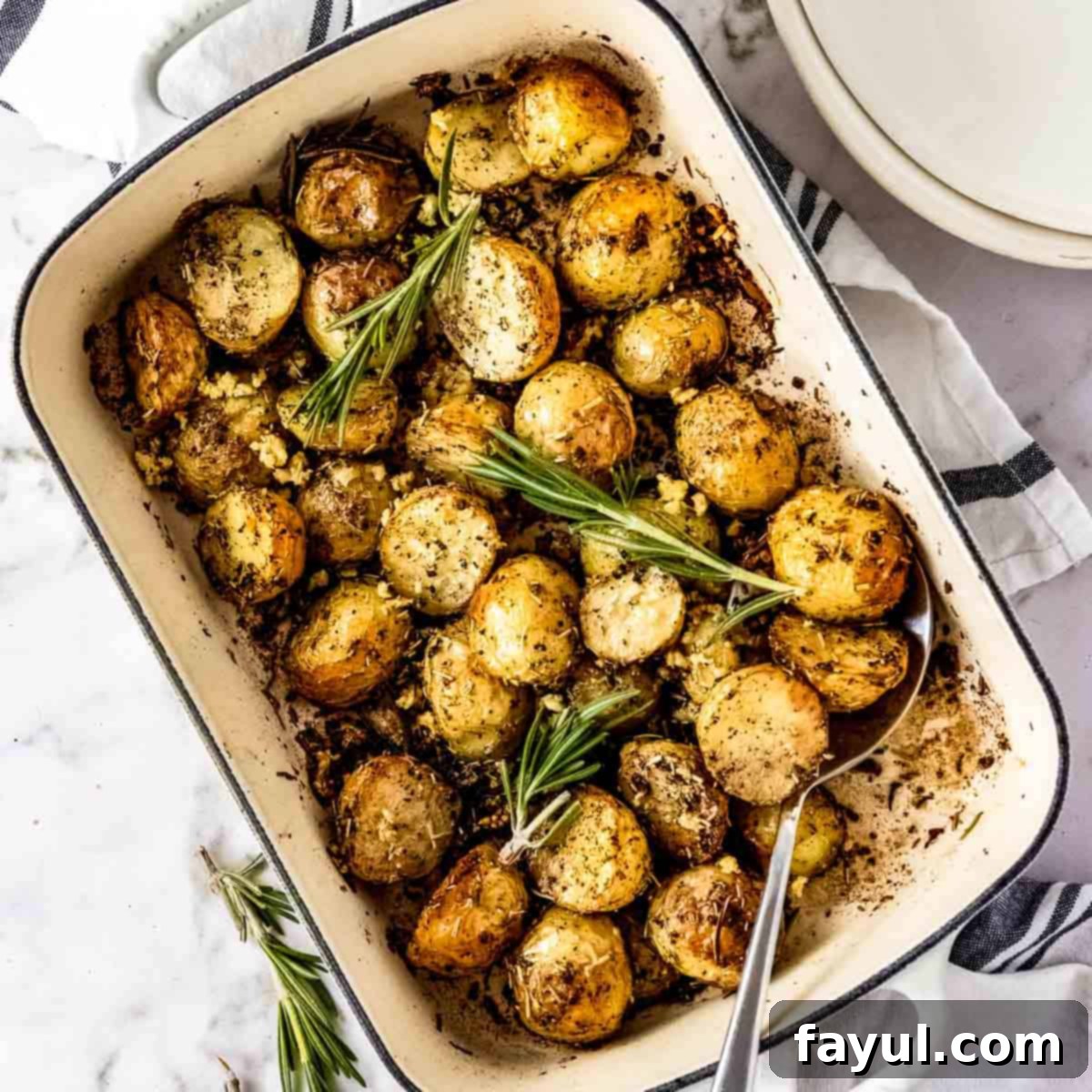 Overhead shot of a white rectangle pan with rosemary potatoes garnished with fresh rosemary with a spoon on the side.