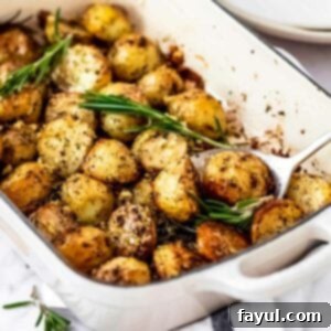 Side shot of a spoon picking up a few potatoes from a white pan garnished with fresh rosemary.