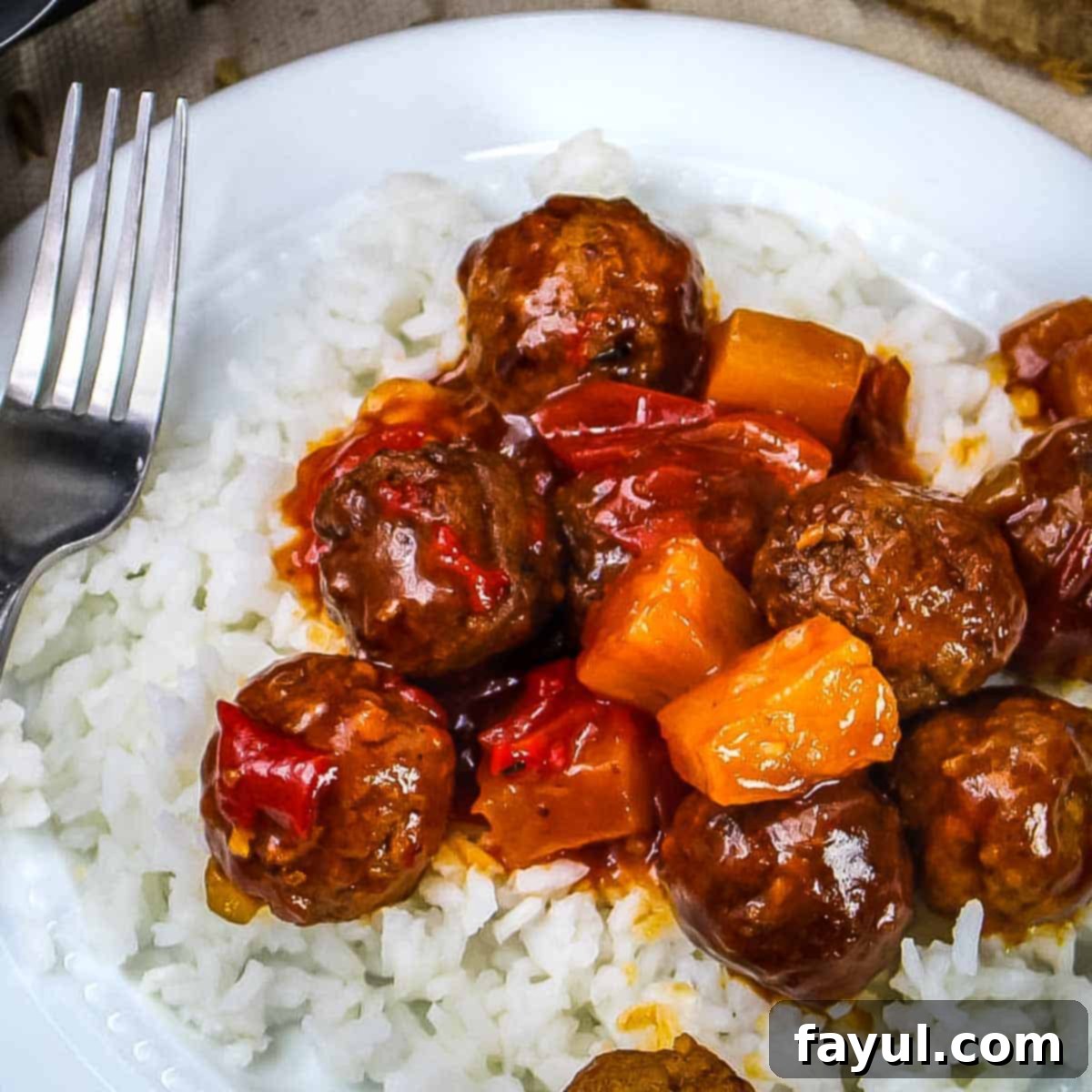 Overhead close-up shot of Hawaiian meatballs served over white rice in a white bowl, with a fork resting on the side, ready to be enjoyed.