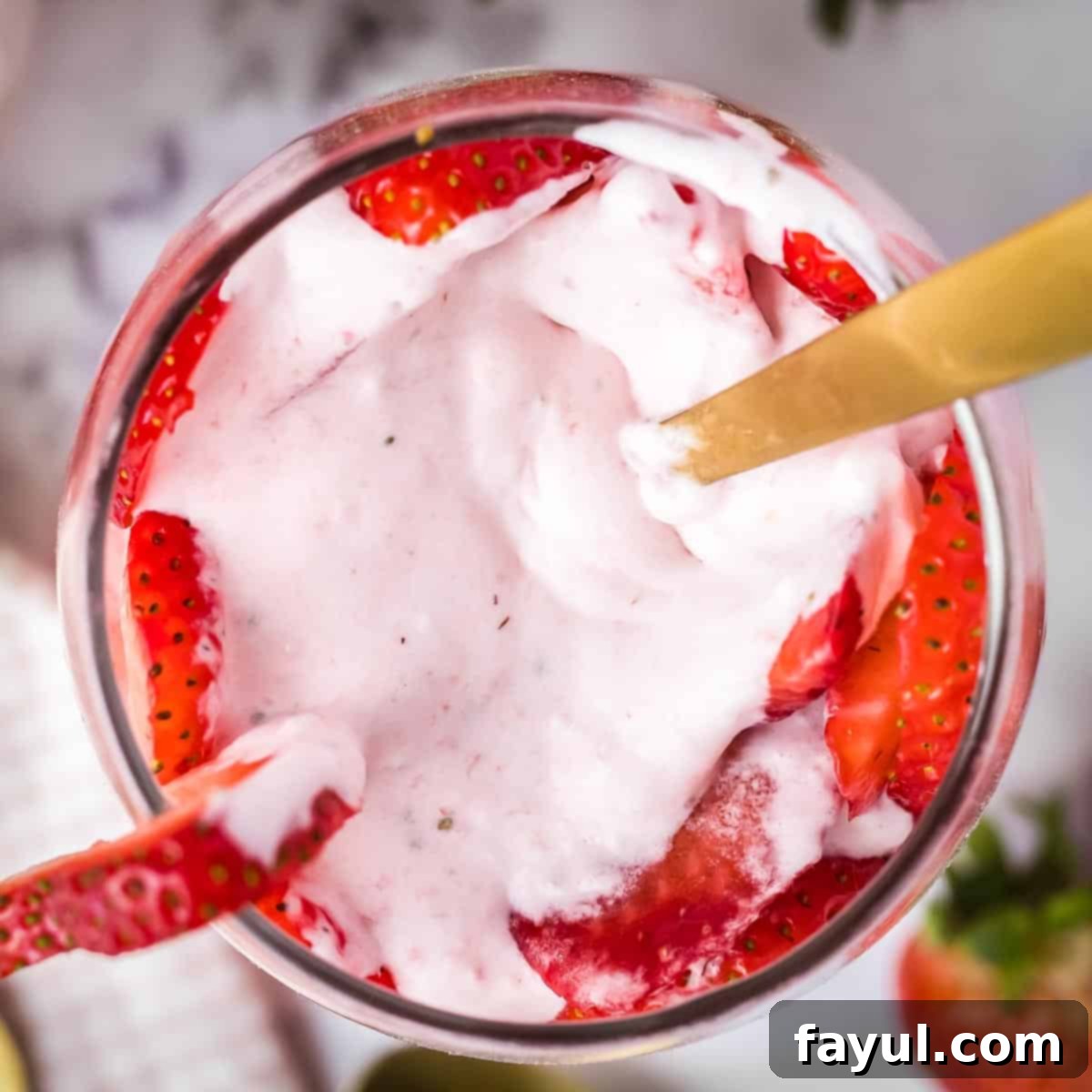 Overhead shot of a glass of strawberry mousse and sliced strawberries with a gold spoon sticking out.