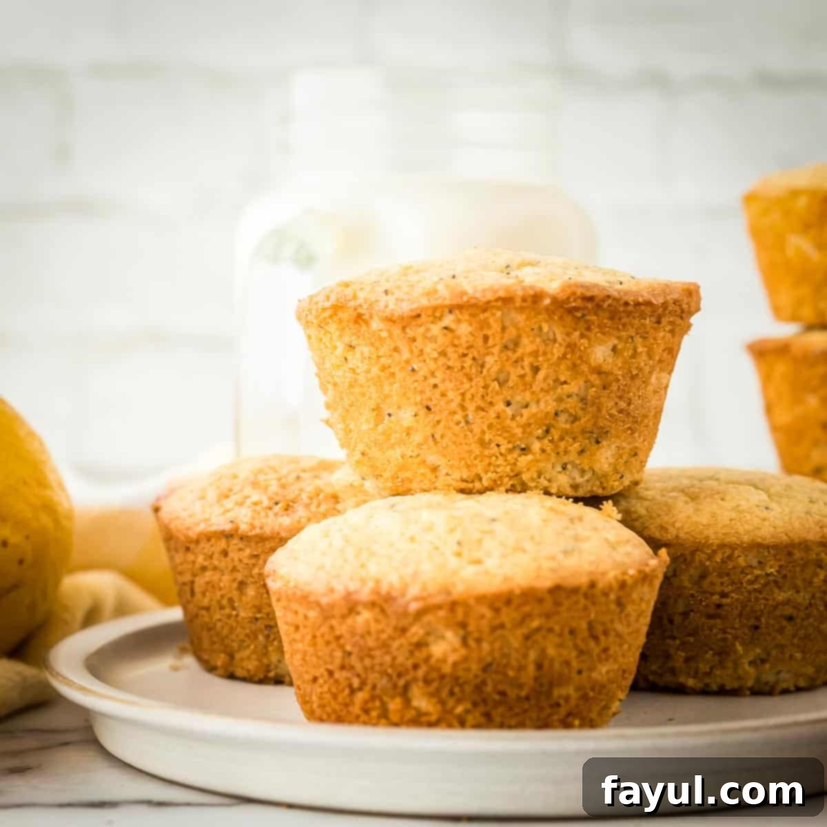 Side shot of lemon muffins stacked on a grey plate with whole lemons in the background.