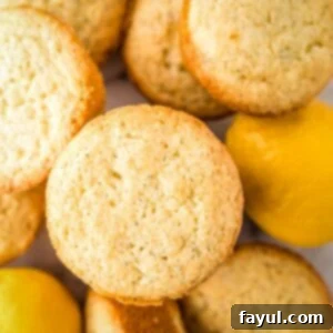 Overhead shot of lemon muffins stacked on a white surface with whole lemons in the background.