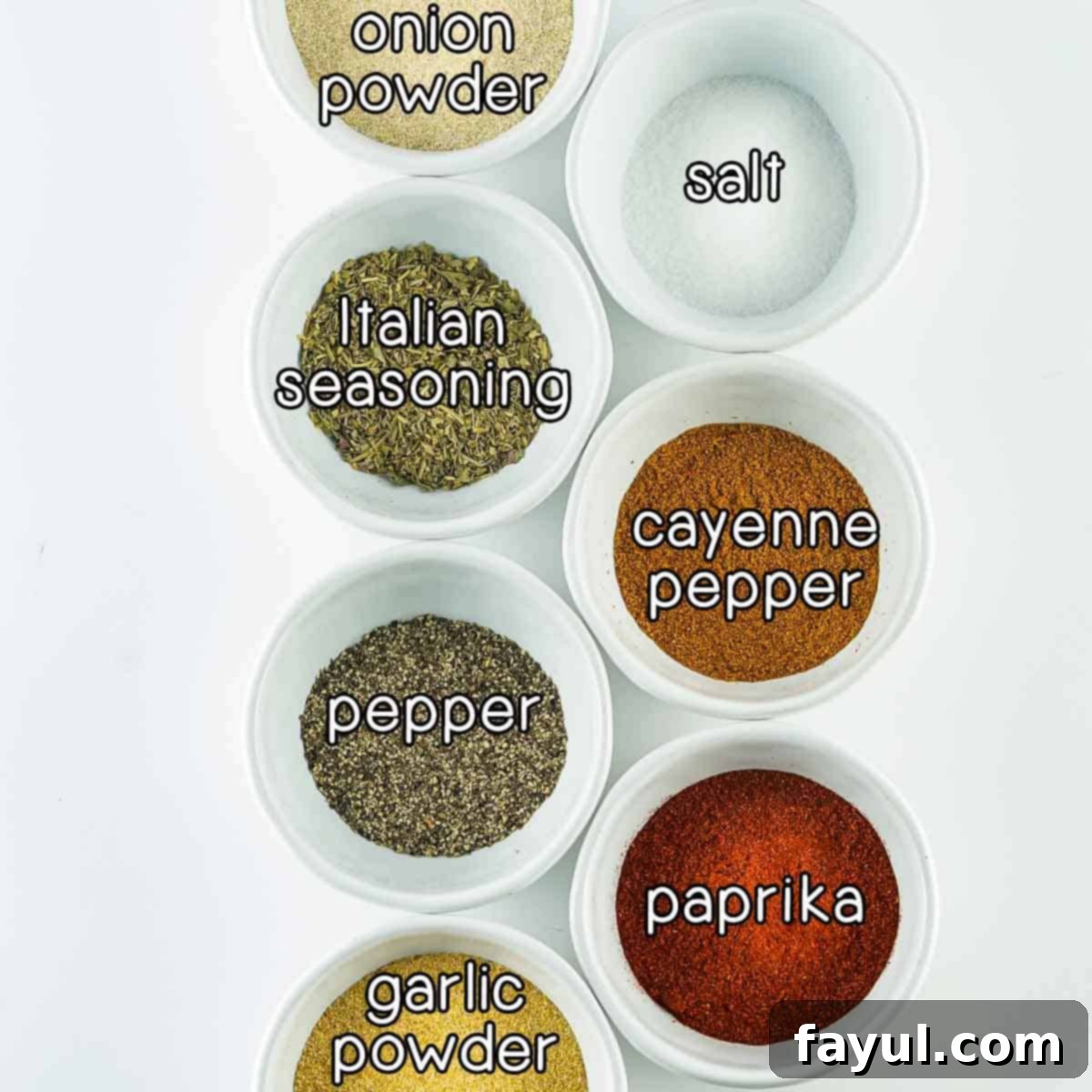 Overhead shot of ingredients including onion powder, Italian seasoning, black pepper, garlic powder, salt, cayenne pepper, and paprika, laid out on a white surface.