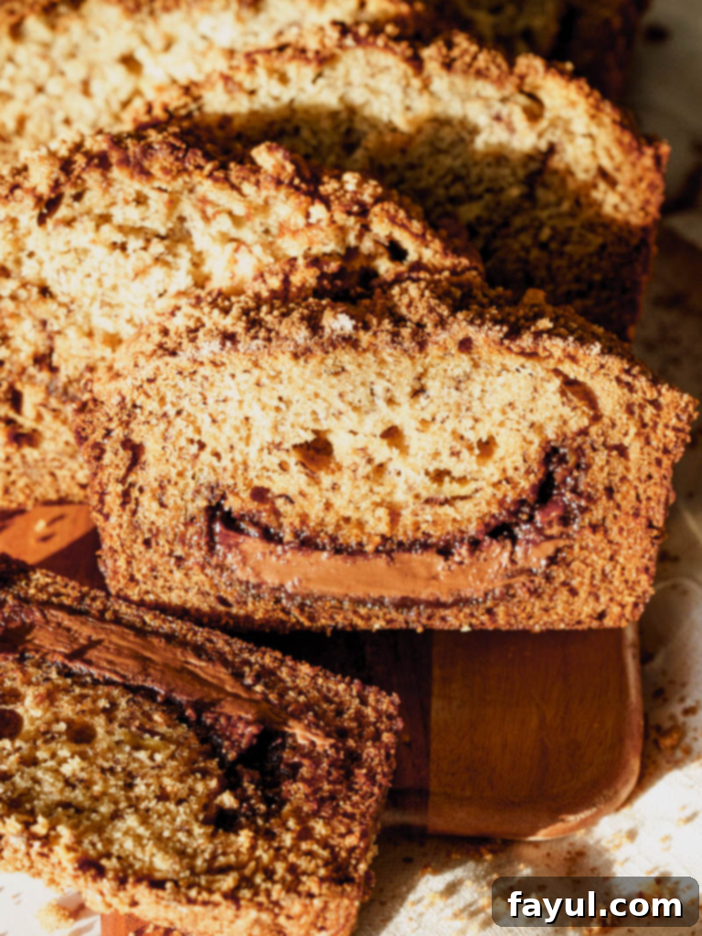 A beautifully sliced loaf of Nutella banana bread, revealing the chocolate hazelnut swirl and cinnamon crumb topping.