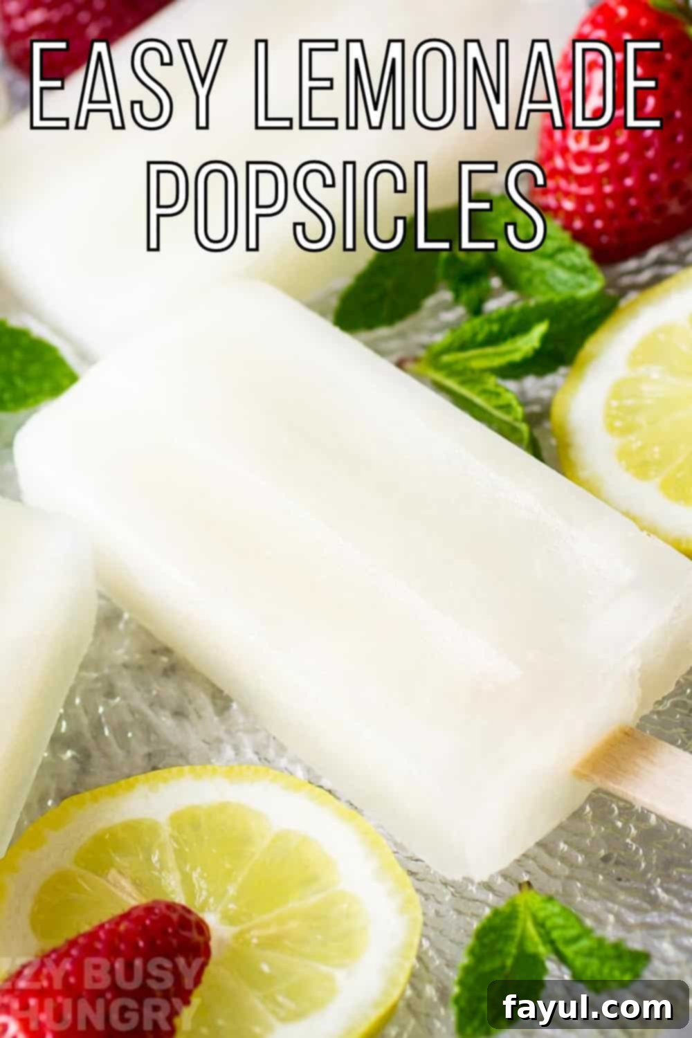 Side shot of lemonade popsicles on a glass plate with mint, lemon slices, and strawberries scattered around.