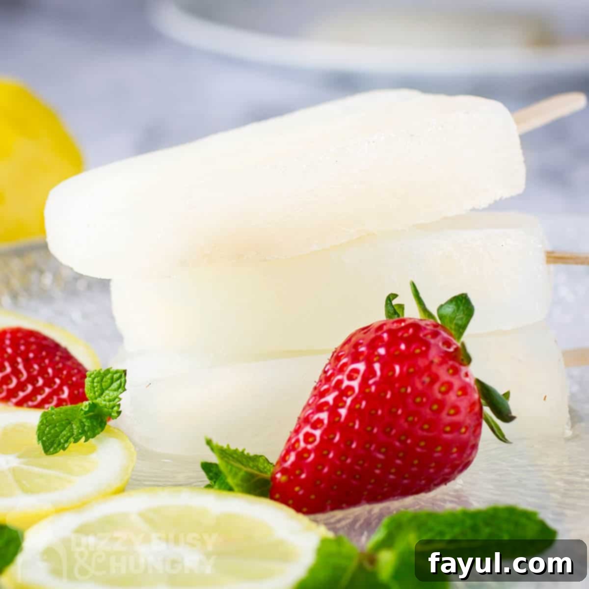 Side shot of three popsicles stacked on each other with strawberries, lemon slices, and mint scattered in front on a glass plate.