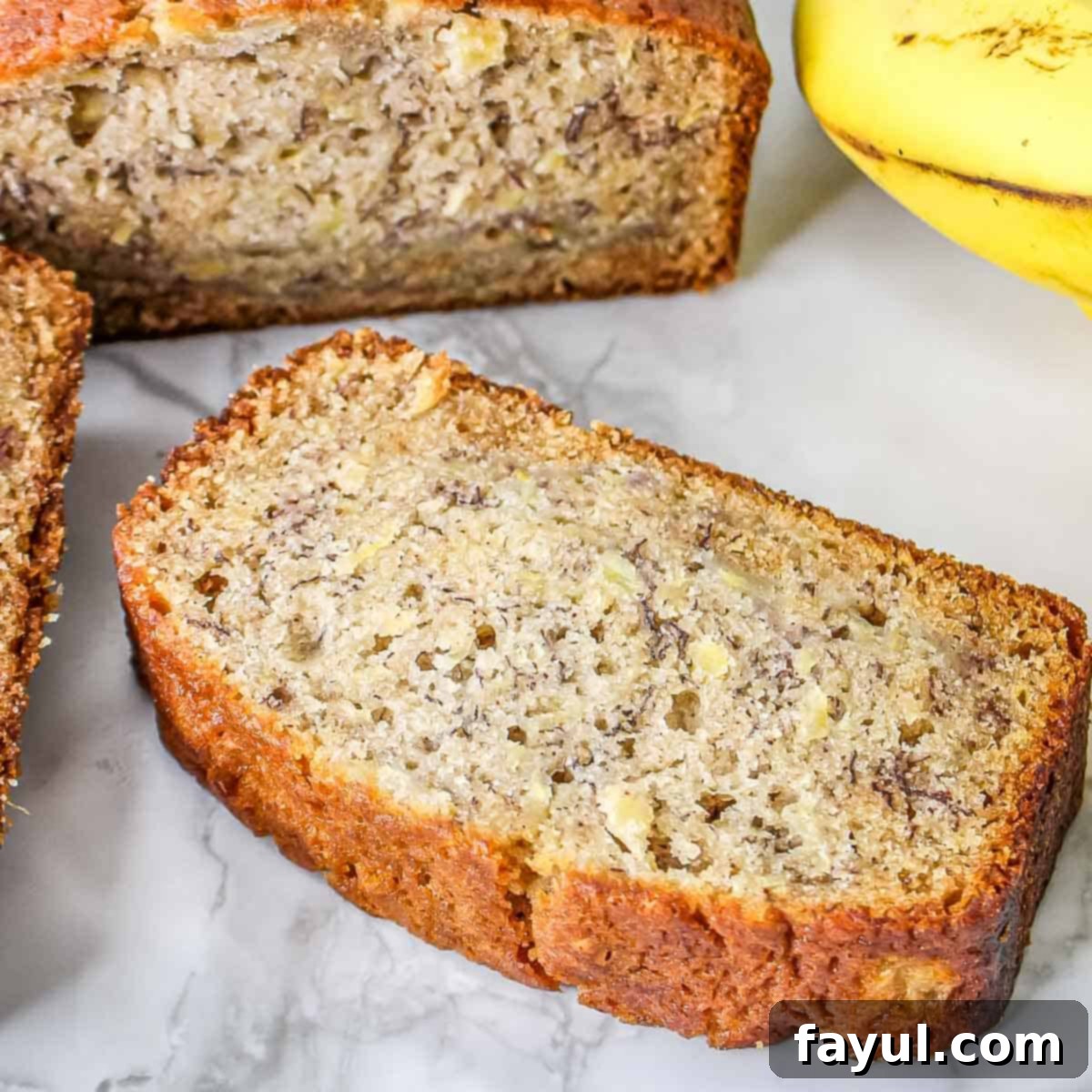 Side close up shot of pineapple banana bread on a marble surface with a banana on the side.