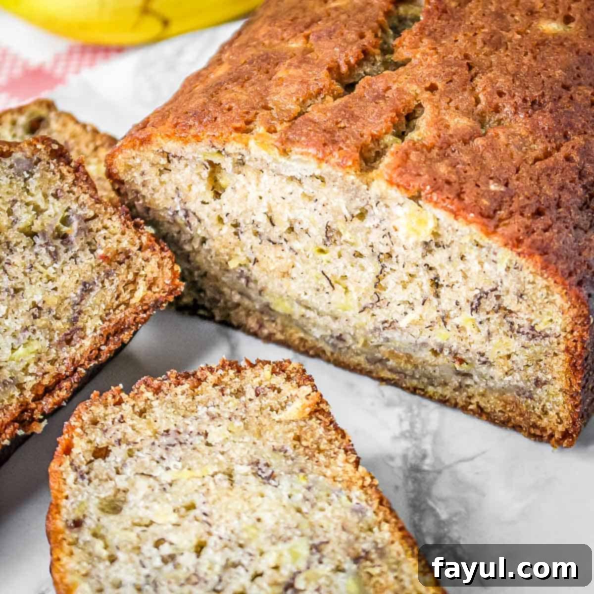 Side shot of whole pineapple banana bread with a few slices on a marble surface.