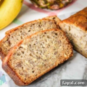Side shot of slices of pineapple banana bread on a marble plate with bananas and a pineapple in the background.