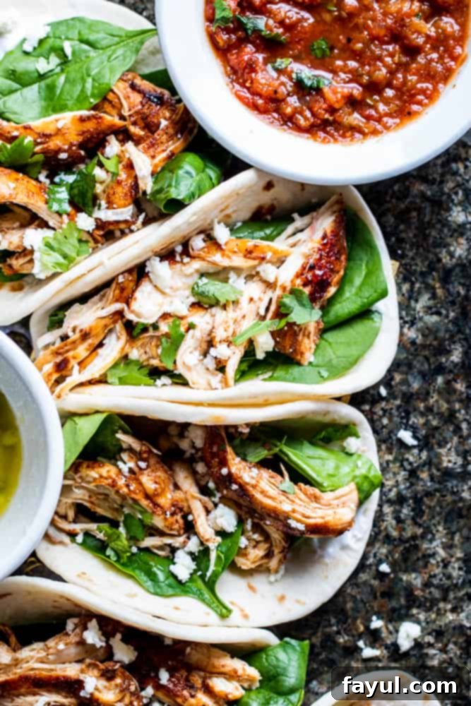 Overhead shot of grilled chicken tacos on a green stone counter with a white bowl of salsa.