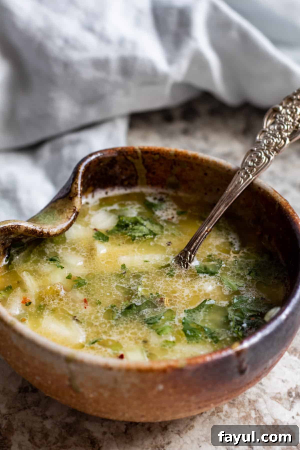 Close up shot of lime butter sauce in brown bowl with silver spoon.