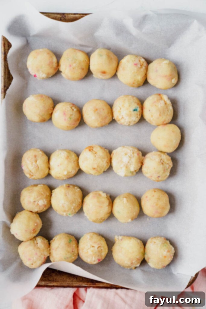 Raw funfetti cake dough rolled into small, uniform balls on a baking sheet, ready for chilling.