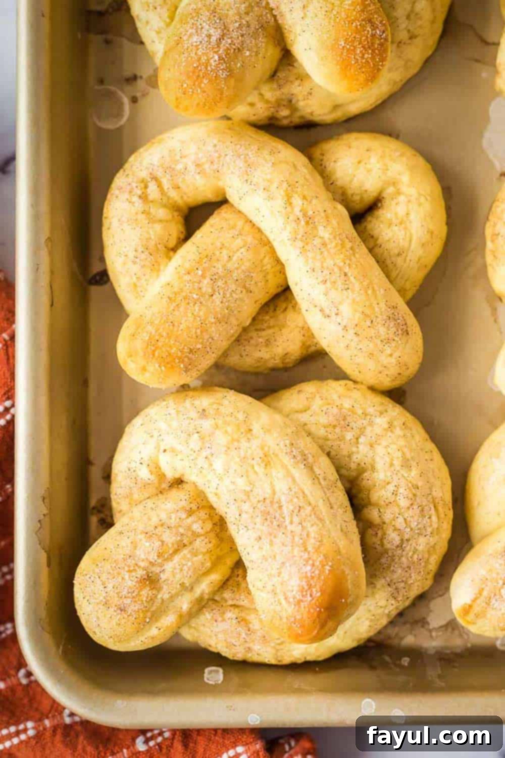 Overhead shot of soft pretzels arranged on a baking sheet with an orange towel on the side.