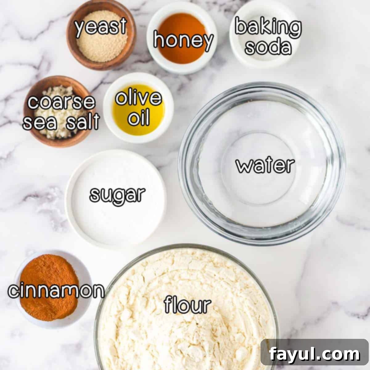 Overhead shot of ingredients - yeast, honey, baking soda, coarse sea salt, olive oil, sugar, water, cinnamon, and flour.