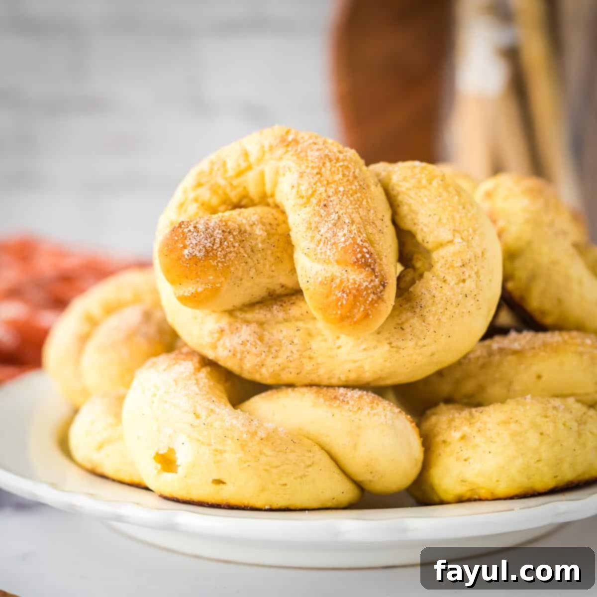 Side shot of multiple pretzels stacked on a white plate on a white surface.