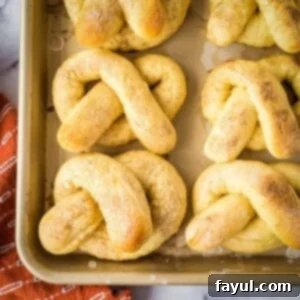 Overhead shot of soft pretzels arranged on a baking sheet with an orange towel on the side.