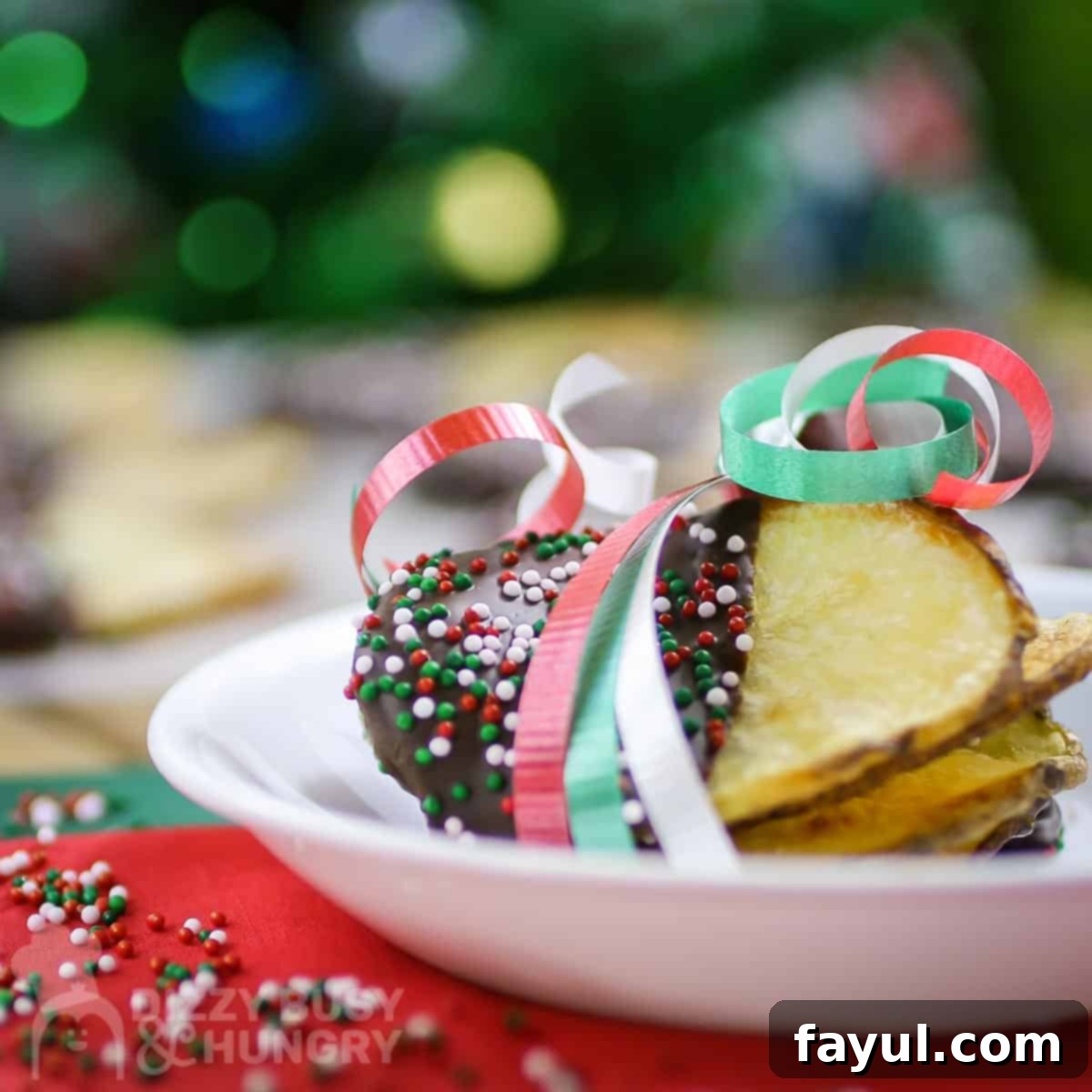 Side shot of multiple chocolate covered potato chips wrapped in red, green, and white ribbon on a small white plate on red and green tissue paper, ready to be served.